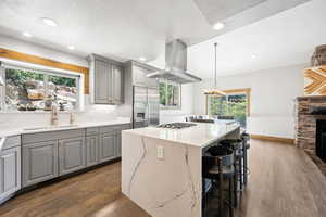 Kitchen with gray cabinets, appliances with stainless steel finishes, island range hood, dark wood-style floors, and a kitchen island