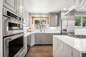 Kitchen with gray cabinets, range hood, stainless steel appliances, healthy amount of natural light, and recessed lighting