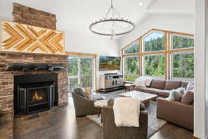 Living room featuring high vaulted ceiling, a stone fireplace, a chandelier, plenty of natural light, and wood finished floors