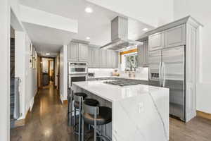 Kitchen featuring stainless steel appliances, gray cabinets, wall chimney range hood, dark wood-style flooring, and recessed lighting