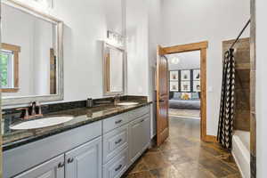 Full bath featuring double vanity, shower / bath combo with shower curtain, connected bathroom, and stone finish floors