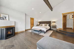 Bedroom featuring wood finished floors, beamed ceiling, a lit fireplace, recessed lighting, and high vaulted ceiling