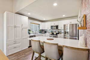 Kitchen featuring appliances with stainless steel finishes, a peninsula, white cabinetry, light wood-type flooring, and recessed lighting