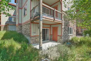 Doorway to property featuring stone siding, board and batten siding, a balcony, and a patio area
