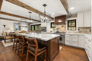 Kitchen with stainless steel appliances, custom exhaust hood, beam ceiling, backsplash, and a center island with sink