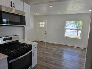 Kitchen with appliances with stainless steel finishes, a textured ceiling, dark wood-style floors, white cabinetry, and recessed lighting