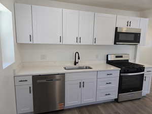 Kitchen with appliances with stainless steel finishes, dark wood-style flooring, white cabinetry, and light stone counters