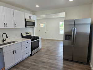 Kitchen featuring stainless steel appliances, recessed lighting, white cabinets, light countertops, and wood finished floors