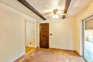 Empty room featuring beamed ceiling, ceiling fan, and a textured ceiling