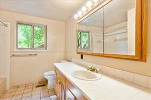 Full bathroom featuring plenty of natural light, vanity, a textured ceiling, a wainscoted wall, and tile patterned flooring