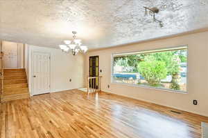 Spare room featuring a chandelier, light wood-type flooring, healthy amount of natural light, and a textured ceiling
