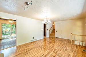 Spare room with wood finished floors, a chandelier, a textured ceiling, and stairs