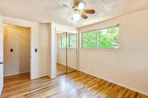 Unfurnished bedroom featuring a textured ceiling, wood finished floors, a closet, and a ceiling fan