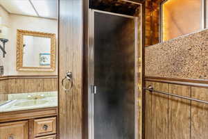 Bathroom with vanity, a shower stall, and wood walls