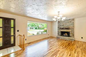 Unfurnished living room featuring wood finished floors, a chandelier, a textured ceiling, and a stone fireplace
