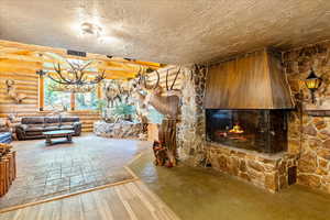 Unfurnished living room with rustic walls, a stone fireplace, wood-type flooring, a chandelier, and a textured ceiling