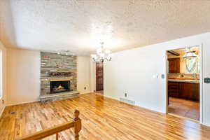 Unfurnished living room with a textured ceiling, light wood-style flooring, a chandelier, and a stone fireplace