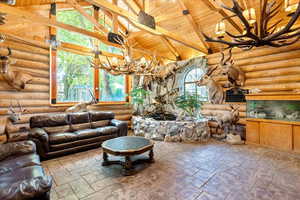 Living area featuring a chandelier, a wood ceiling with exposed beams, high vaulted ceiling, rustic walls, and stone tile flooring