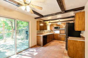 Kitchen with appliances with stainless steel finishes, brown cabinets, a textured ceiling, beamed ceiling, and a ceiling fan