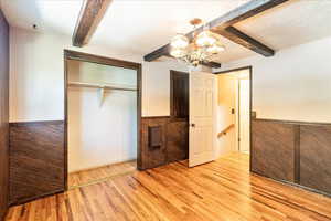Unfurnished bedroom with beamed ceiling, a chandelier, light wood finished floors, a wainscoted wall, and a closet
