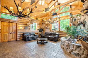 Living area with a chandelier, high vaulted ceiling, a wooden ceiling with exposed beams, log walls, and stone finish flooring