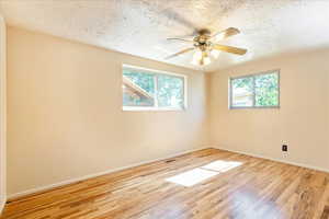 Unfurnished room with healthy amount of natural light, wood finished floors, ceiling fan, and a textured ceiling