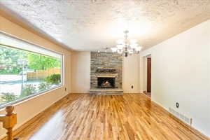 Unfurnished living room featuring light wood-type flooring, a chandelier, a stone fireplace, and a textured ceiling