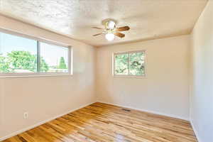 Spare room featuring light wood-type flooring, a ceiling fan, and a textured ceiling