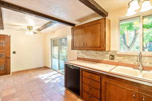 Kitchen with a textured ceiling, dishwasher, beam ceiling, light countertops, and brown cabinetry