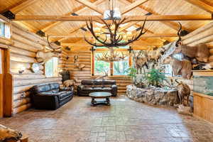 Living room with a chandelier, wood ceiling, stone tile flooring, and log walls