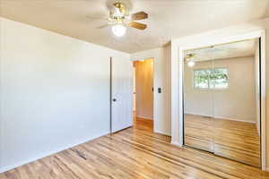 Unfurnished bedroom featuring a closet, light wood-type flooring, a textured ceiling, and a ceiling fan