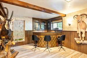 Indoor dry bar featuring beam ceiling, a wainscoted wall, wood finished floors, a textured ceiling, and wood walls