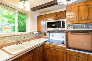 Kitchen with stainless steel microwave, wall oven, tasteful backsplash, brown cabinetry, and beam ceiling