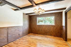 Empty room with wood finished floors, wooden walls, a chandelier, beamed ceiling, and a wainscoted wall