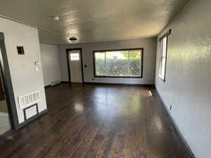 Unfurnished living room featuring dark wood-type flooring and baseboards