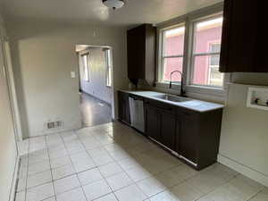 Kitchen with stainless steel dishwasher, light countertops, and light tile patterned floors