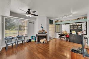 Living room with ceiling fan, a textured ceiling, wood finished floors, and a high end fireplace