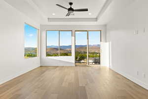 Empty room featuring a mountain view, a tray ceiling, light wood-type flooring, a ceiling fan, and recessed lighting