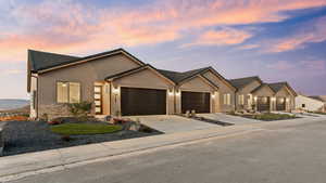 View of front facade with an attached garage, stone siding, stucco siding, and driveway