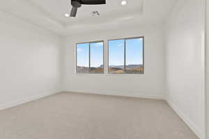 Empty room with a raised ceiling, ceiling fan, light carpet, and recessed lighting