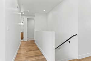 Hallway with an upstairs landing, recessed lighting, and light wood-style flooring