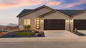 View of front of house featuring a garage, stucco siding, driveway, stone siding, and a tile roof