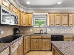 Kitchen with black appliances, stone counters, ornamental molding, and decorative backsplash
