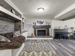 Living area featuring a textured ceiling, wood finished floors, and a fireplace with raised hearth