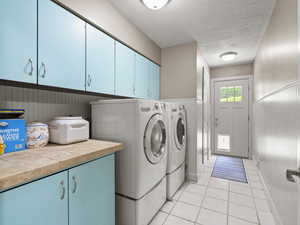 Laundry room featuring cabinet space, washing machine and dryer, a textured ceiling, light tile patterned floors, and a wainscoted wall