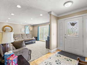 Foyer featuring ornamental molding, a textured ceiling, light wood-style flooring, and recessed lighting