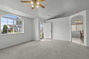 Carpeted empty room featuring a chandelier, healthy amount of natural light, ceiling fan, lofted ceiling, and arched walkways