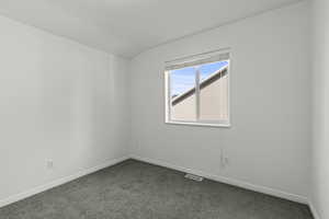 Unfurnished room featuring dark colored carpet and lofted ceiling