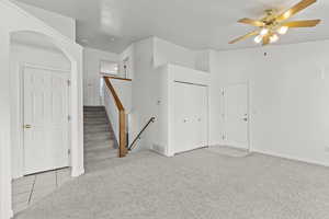 Tiled spare room featuring carpet floors, a ceiling fan, arched walkways, and stairs