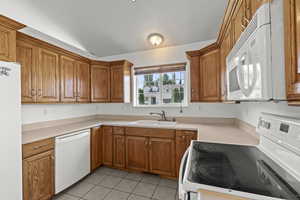 Kitchen with white appliances, lofted ceiling, brown cabinets, light tile patterned flooring, and light countertops